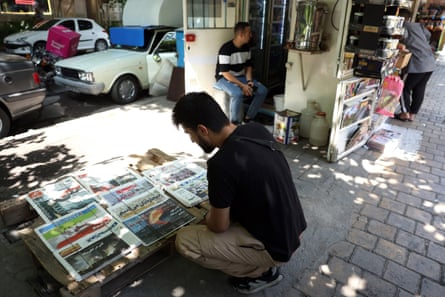 A man crouches to look at Iranian newspapers at a newsstand