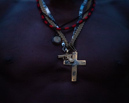 An up-close photo of a man’s chains, including a gold, worn gun, a cross and red-and-black necklace.