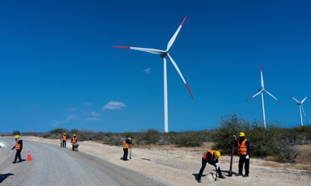 Six men in h-vis jackets working along a road, with three turbines looming over them