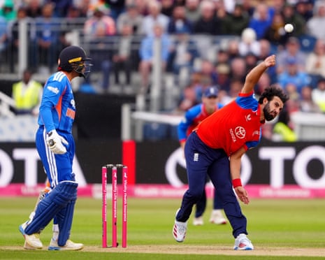England's Saqib Mahmood in a red and blue uniform bowls while a batsman in blue watches