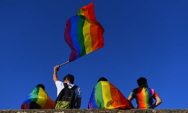 Four people with rainbow flags resting against a wall