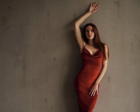 Margarita Reutt in a red satin dress leans against a wall with one arm raised overhead