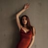 Margarita Reutt in a red satin dress leans against a wall with one arm raised overhead
