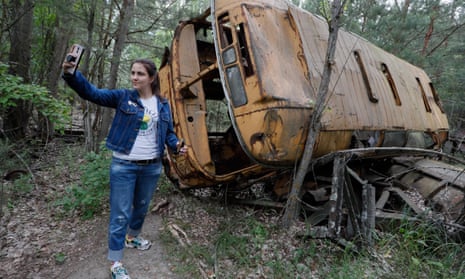 A visitor takes a selfie with an abandoned bus during a tour in Chernobyl