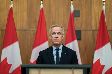 A man in a suit at a lectern standing in front of a row and red-and-white Canadian flags.