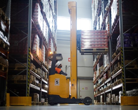 A warehouse worker uses a reach forklift to load pallets laden with goods