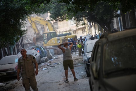 a man reacts as he watches an excavator remove debris on a street