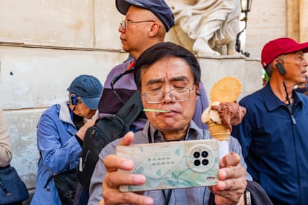 A tourist takes a selfie in front of the fountain while holding an ice-cream