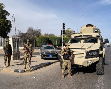 Armed men stand near a military vehicle at a road junction