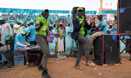 Two men dance at an election rally surrounded by supporters wearing turquoise clothing