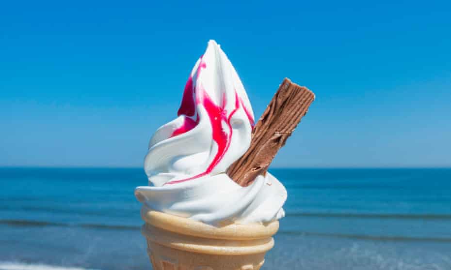 A soft-serve ice-cream with a half-size Flake & strawberry sauce, against a blue sea and sky