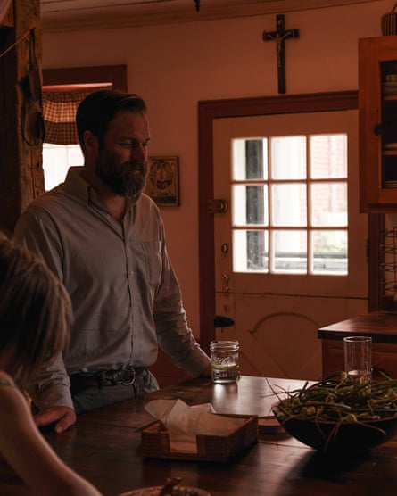 A man stands over a dining table as a cross hangs over the doorway in the background