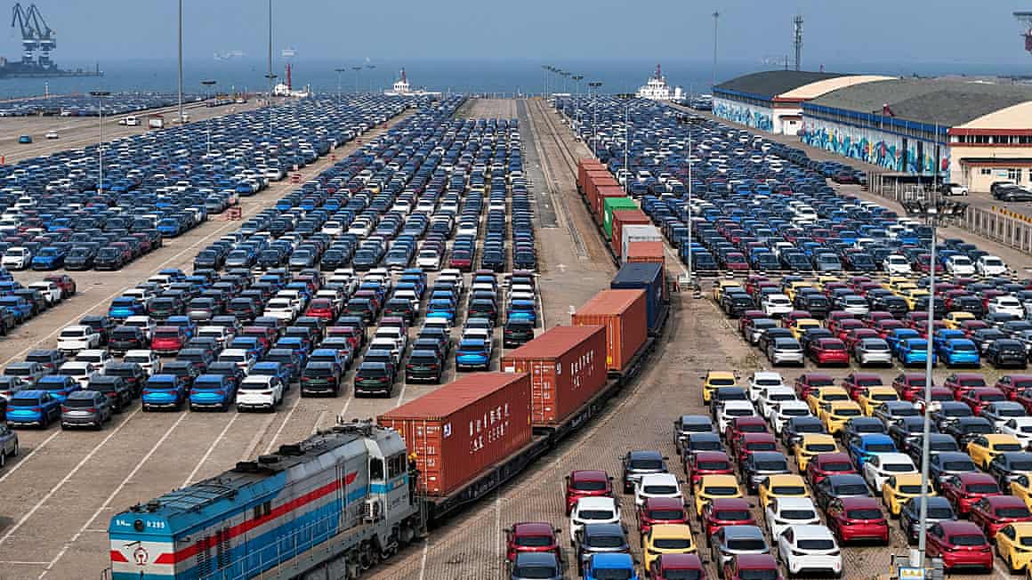 Aerial image of a cargo train moving past new cars waiting for shipment in a port