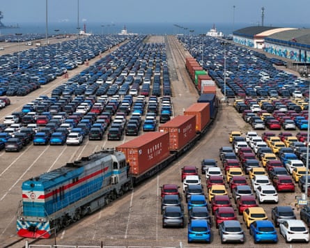 A cargo train moves past new cars waiting for shipment in a port, in Yantai in east China’s Shandong province