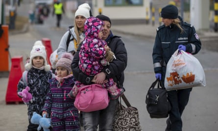 A border patrol guard helps refugees, mostly women with children, arriving at the Polish border crossing in Medyka