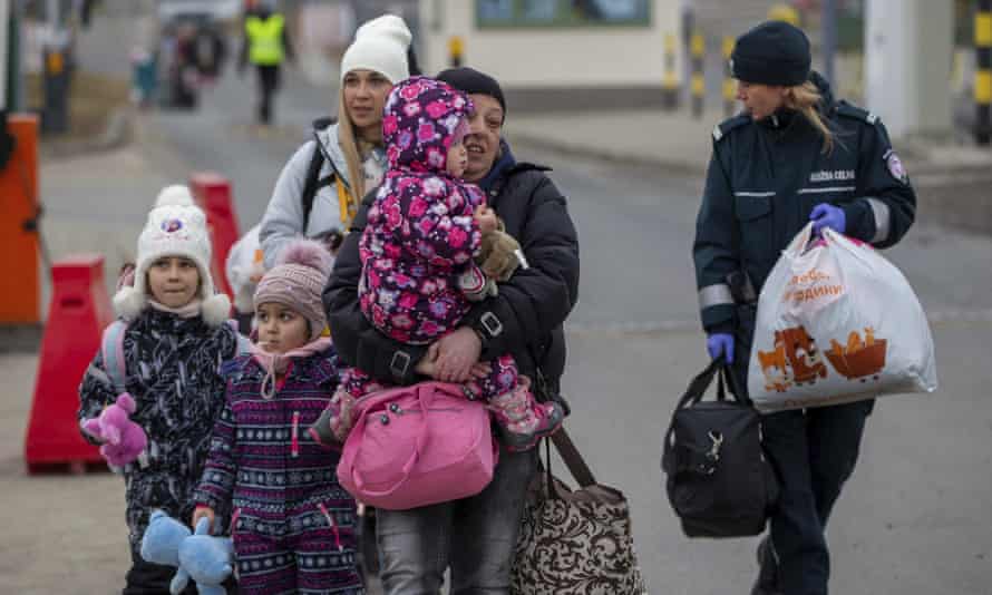 A border patrol guard helps refugees, mostly women with children, arriving at the Polish border crossing in Medyka