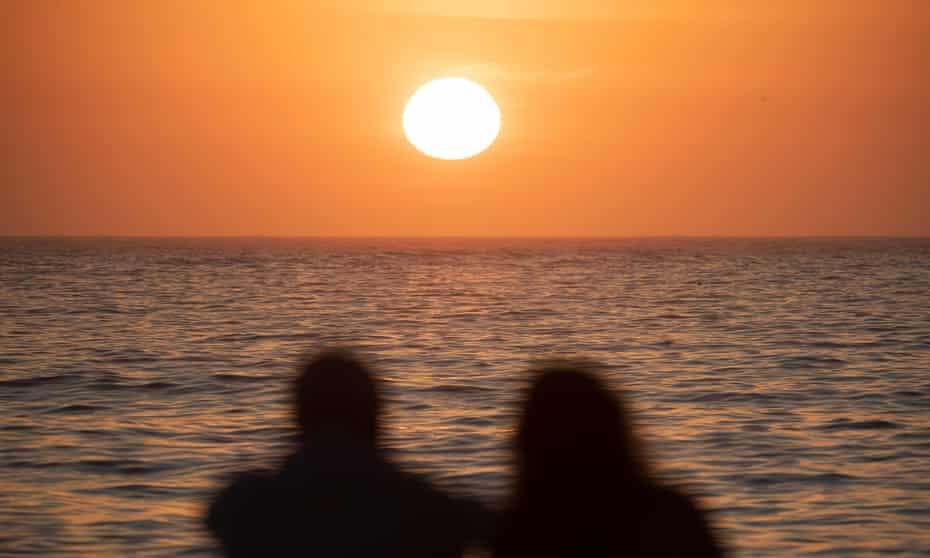silhouettes of two people looking at the sun rise over the ocean's horizon