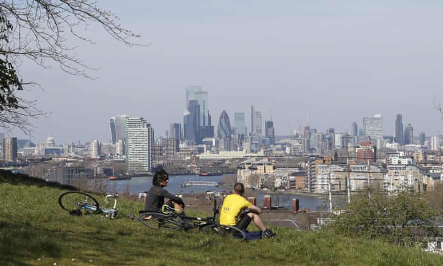 Cyclists sit on the upper slopes of Greenwich Park overlooking the London skyline.