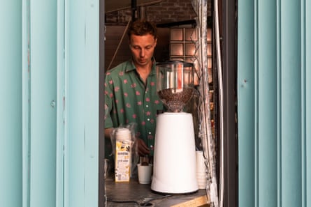 A barista seen at work next to a bean grinding machine through the destroyed window of his cafe