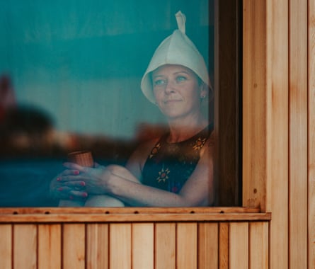 A woman wearing a swimming costume and a sauna cap sitting in a sauna looking out of a window