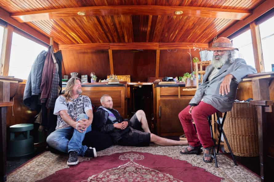 Brian Doris, left, the homeless coordinator Robbie Powell, center, and Jeff Jacob Chase, right, talk in Doris’s boat.