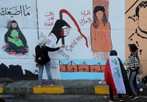 Anti-government protesters stand near graffiti messages that say ‘Iraqi women said no to the tyrants,’ and ‘I will not waste you,’ near Tahrir Square.