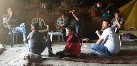 A family sits on rugs in a stone-floored cave, while McKernan writes in a notebook