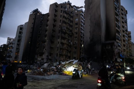 लोग काली पड़ी और क्षतिग्रस्त ऊंची इमारतों के पास इकट्ठा होते हैं।