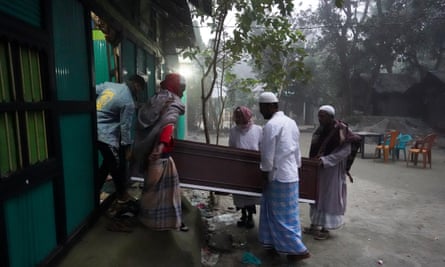 Five men carry a coffin out of a house.
