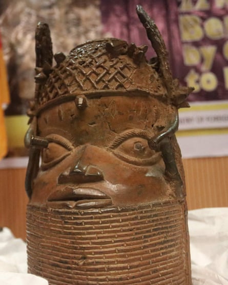 A stylised bronze sculpture of a head with an extended beaded collar covering the chin, and bead clusters on the head