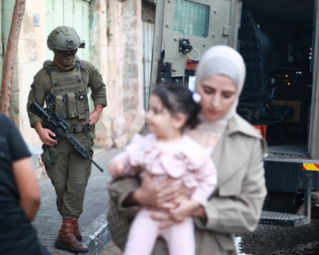 Israeli soldiers standing guard in an alleyway in Hebron, West Bank, as a mother and baby walk past