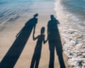 Shadow on sandy beach of a family of three holding hands