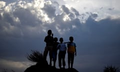 Four boys stand on a hill silhouetted against a dark sky