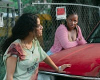 Three young people lean on a car in a car park. One woman's shirt is bloodied