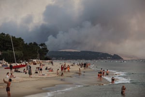People swim on the Moulleau’s beach as smoke rises from the forest fire in La Teste-de Buch