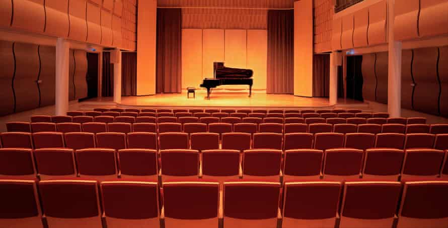 A piano on stage inside an empty concert hall