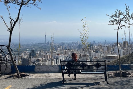 A woman sits on a bench overlooking a city.