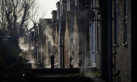 The backs of a row of Victorian terraced houses, lit weakly by the sun through the branches of bare trees, with clouds of smoke from numerous gas boiler exhausts visible all along the row