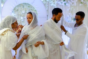 A bride and groom have their white robes adjusted by a man and woman, also dressed in white robes