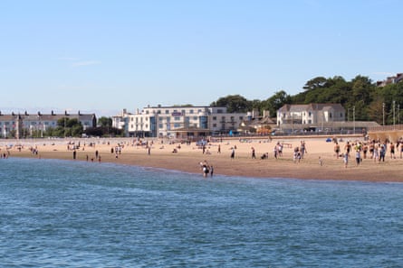 View from the sea towards people on the beach on a warm day. A few people are paddling