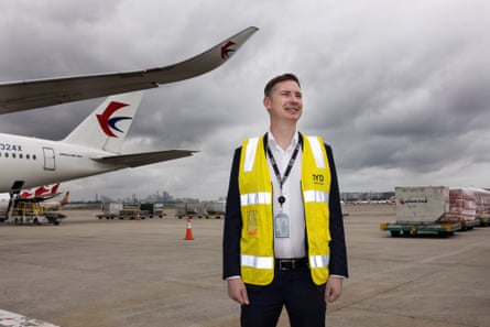 Greg Hay stands in front of a plane, wearing a yellow vest 
