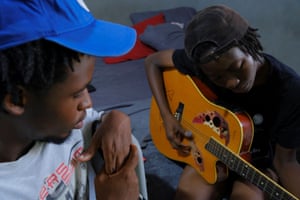Harmonie Bataka plays the guitar as her best friend, Tommy Taylor, listens and watches, at home.