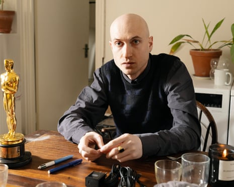 Daniel Blumberg sitting at his messy kitchen table, on which sits his gleaming Oscar