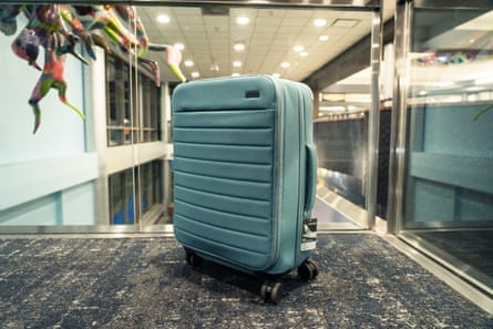 A teal-colored suitcase in an airport by glass barrier