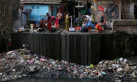 People fill water containers and wash their clothes from municipal water pipes alongside a polluted water channel in Kolkata, India.
