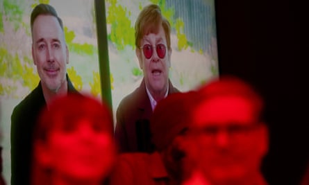 Elton John and David Furnish on a screen in the background with Keir Starmer and Angela Rayner under a red light in the foreground