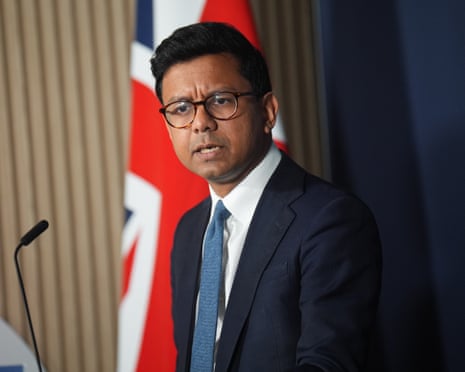 Kanishka Narayan speaks standing in front of a furled union jack flag. He is in his mid-30s and wears glasses, a dark blue suit and blue tie.