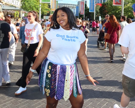 Whitney Jones stands in front of Wembley stadium surrounded by other people attending the harry Styles concert. She wears a T-shirt that reads ‘Get some taste’ and a skirt made from neck ties.