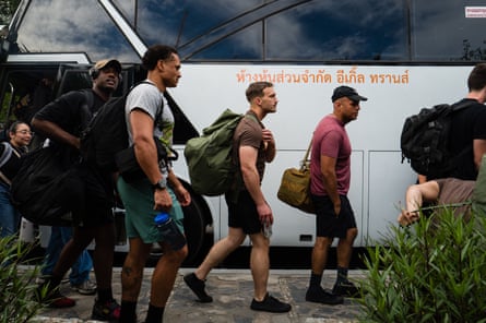 Young men with duffel bags walk next to a bus.