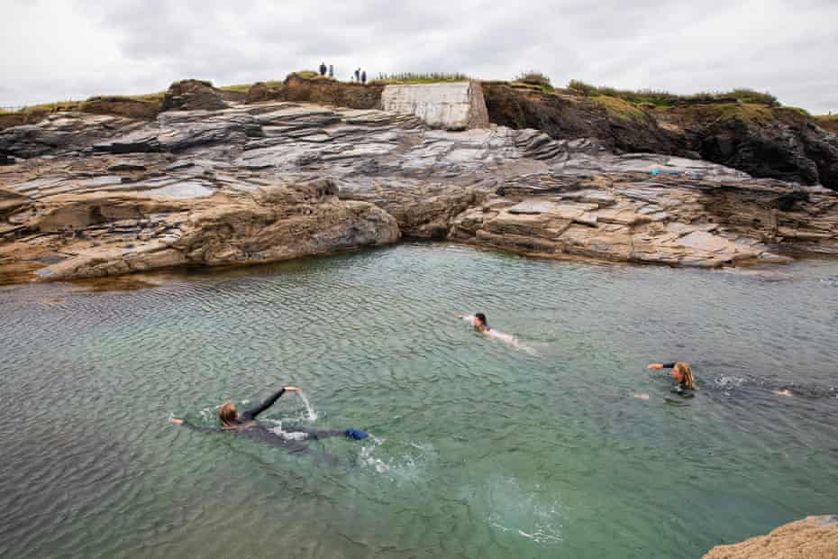 Three people swimming towards the rocky edge of the ocean pool